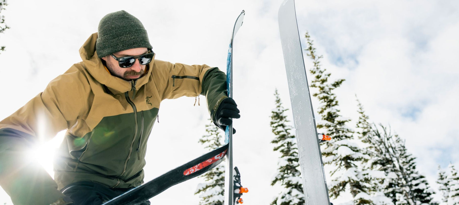 person in green jacket and toque putting climbing skins on skis