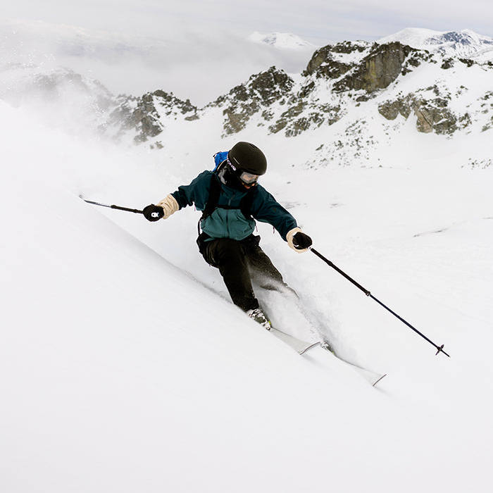 skier skiing down steep incline holding poles and rocky mountains in background