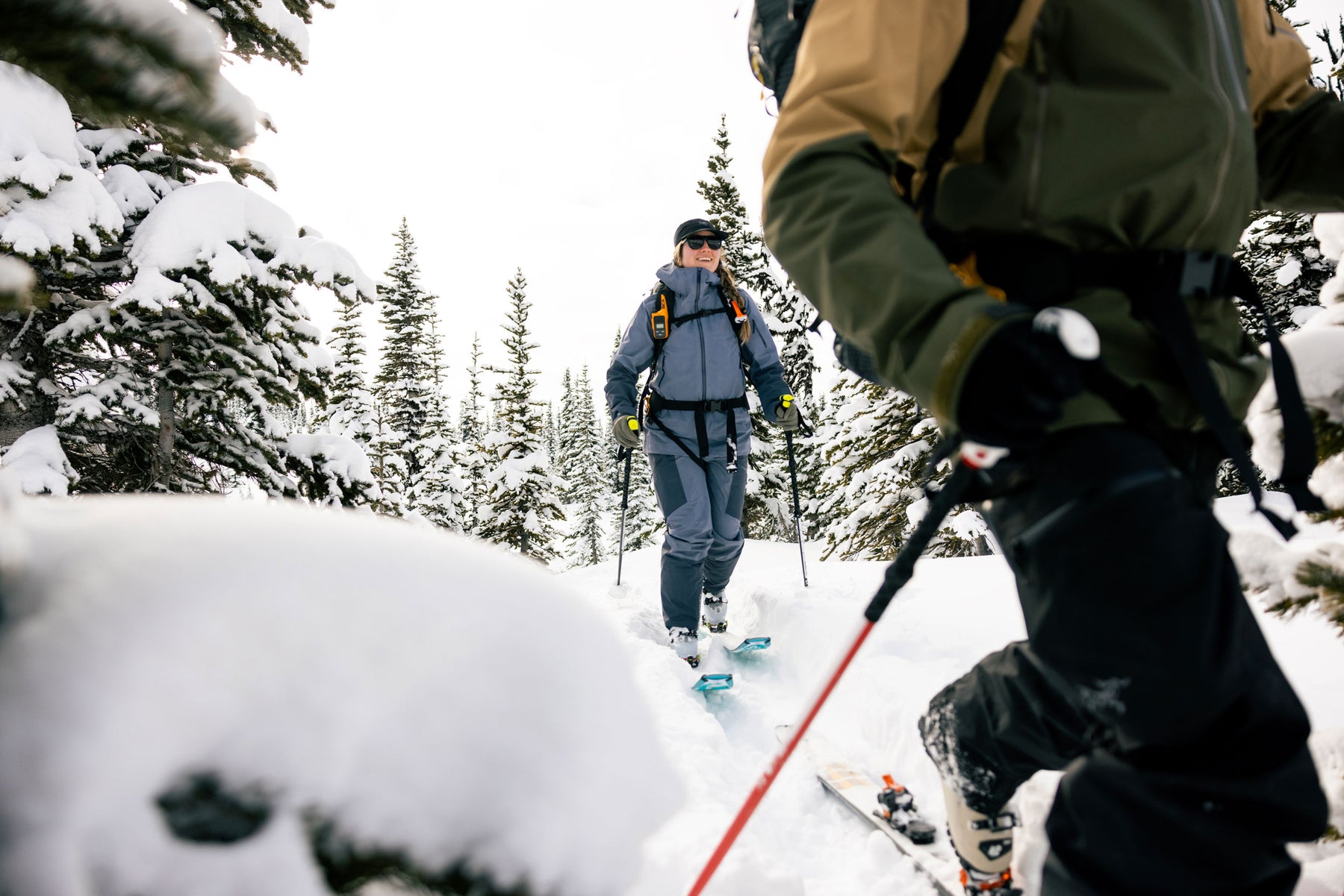Two people skiing through a snowy forest with trees and snow-covered ground.